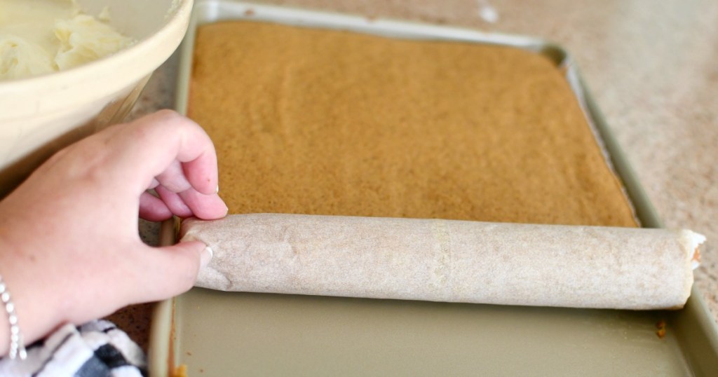 rolling up a pumpkin cake in parchment paper