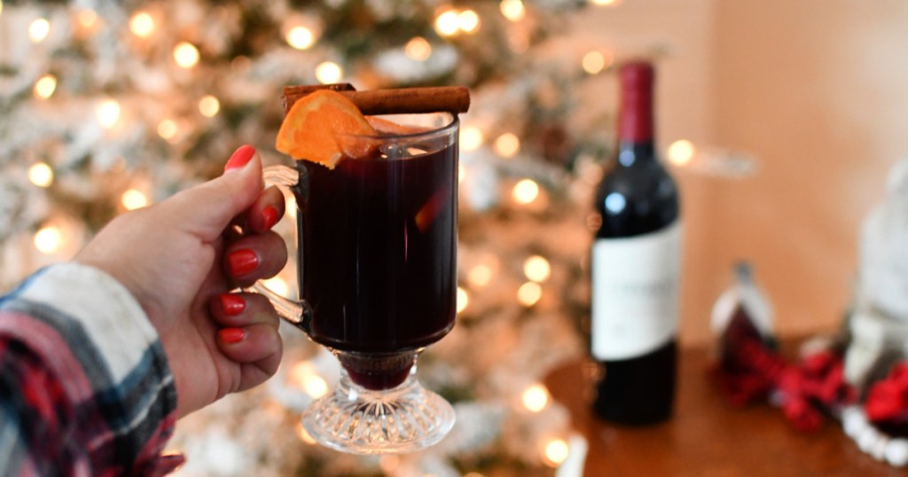 holding a glass of mulled wine by the tree