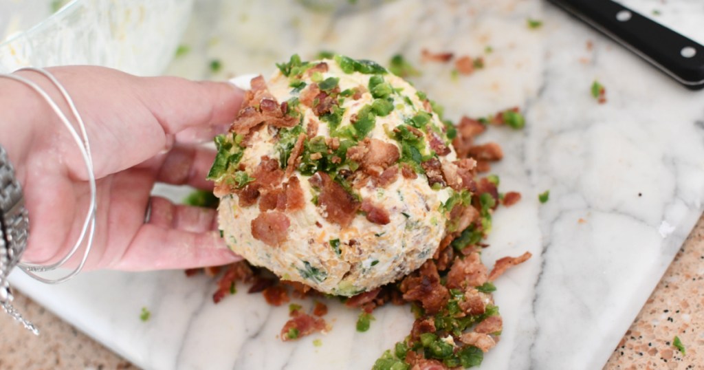 rolling a cheeseball in bacon and jalapeno