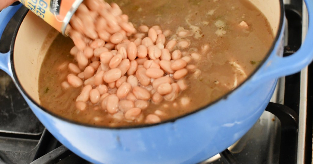 pouring white northern beans into white chili
