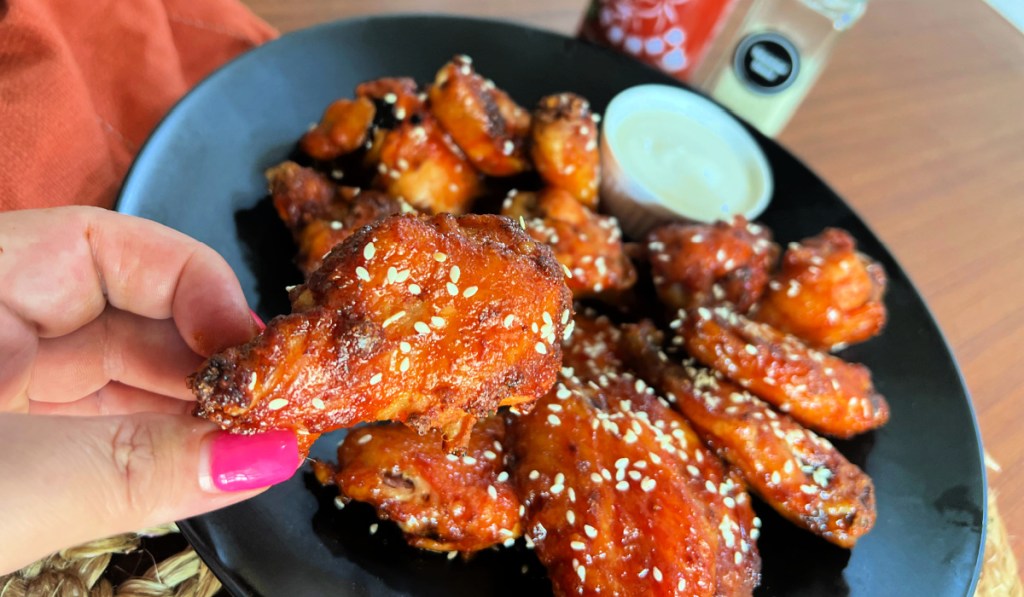 holding a sweet and spicy honey sriracha chicken wing on a plate 