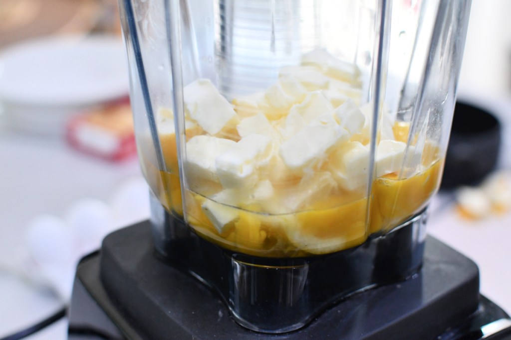 Adding cut up butter to the blender with lemons and eggs. 