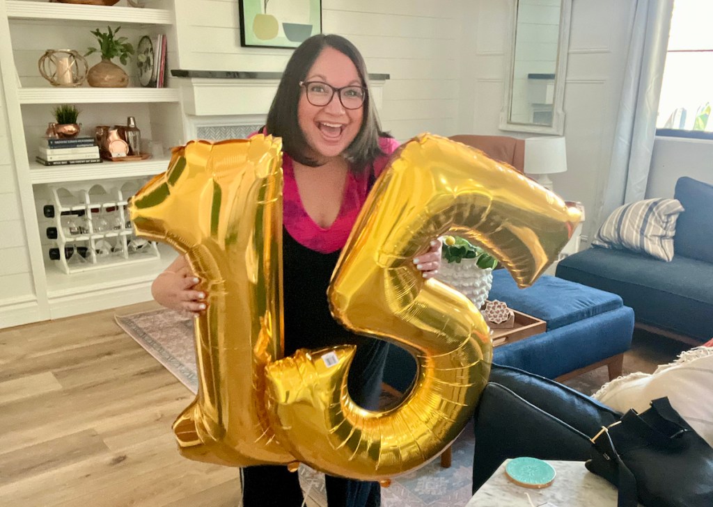 woman holding jumbo size gold foil 15 balloons in living room