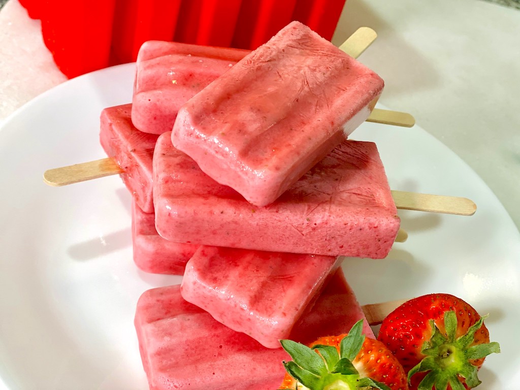 popsicles stacked on one another with fresh strawberries on plate