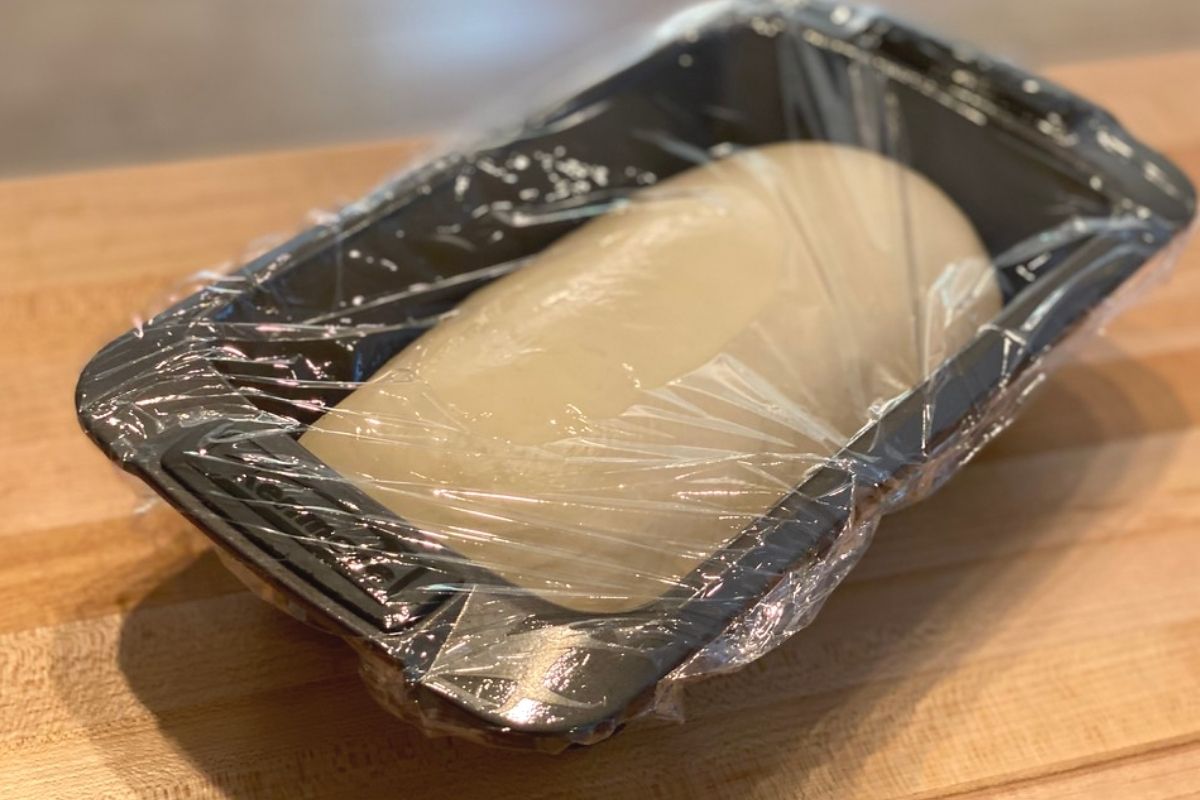Bread dough in a bread pan covered with saran wrap