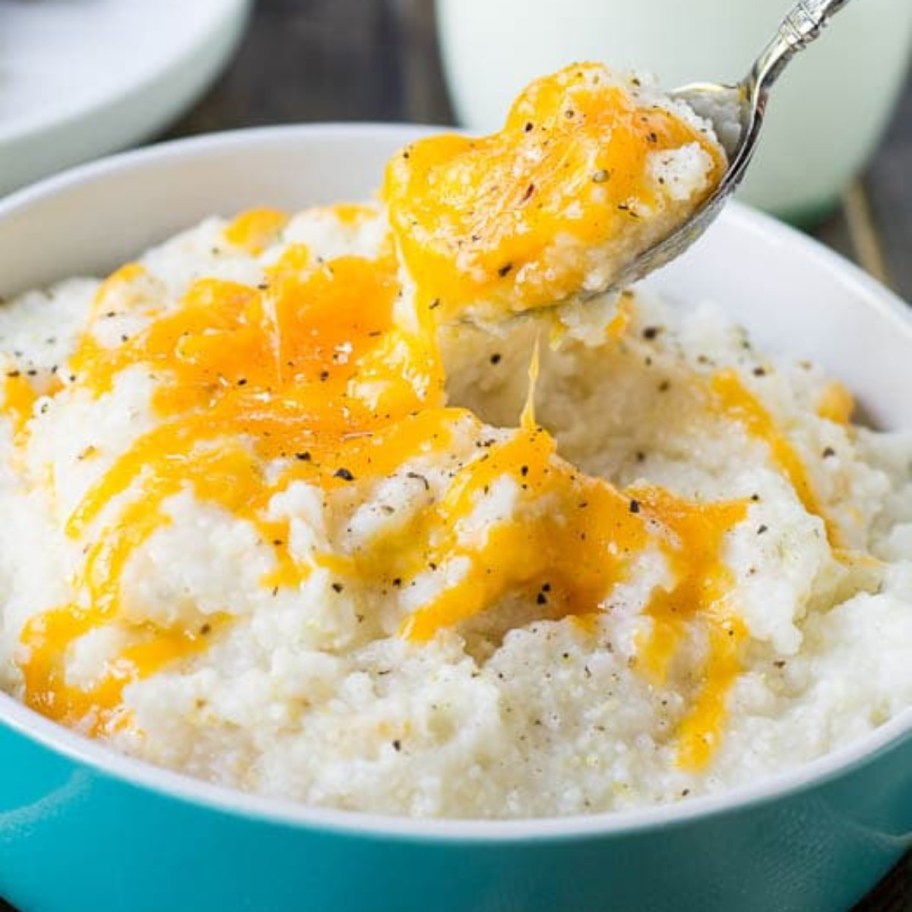 spooning cheesy grits from a blue bowl