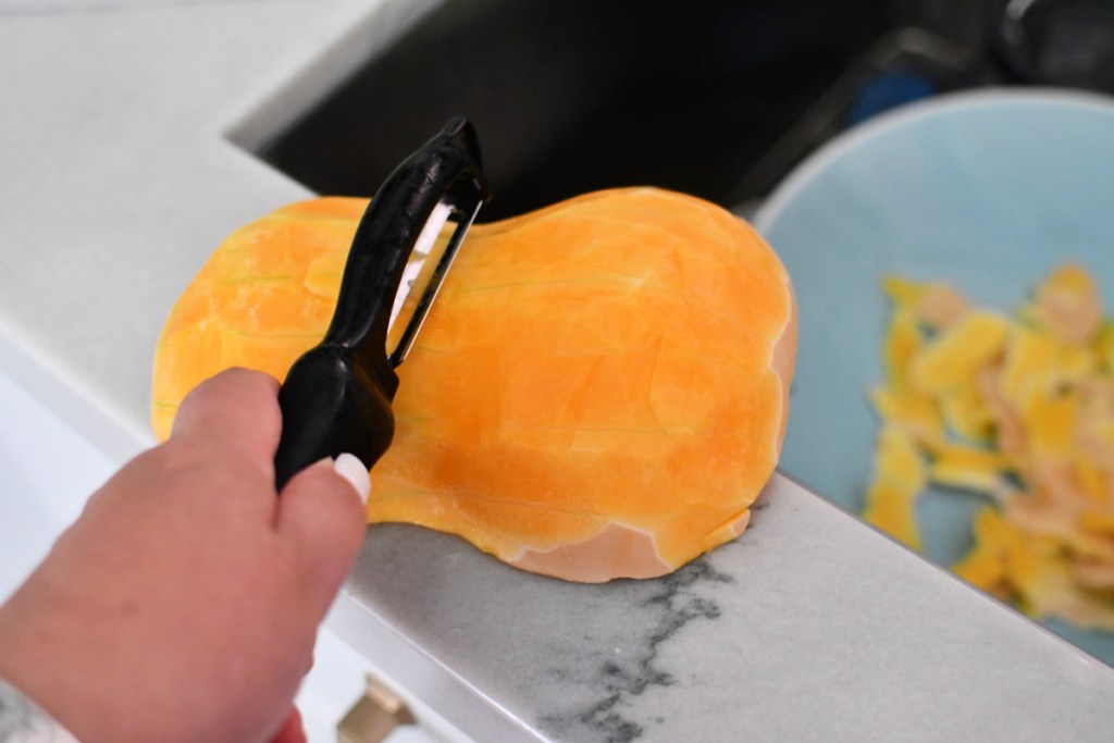 peeling a butternut squash next to sink for soup