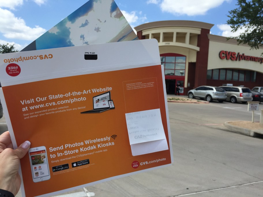 woman's hand pictured holding up a CVS photo envelope in front of a CVS store