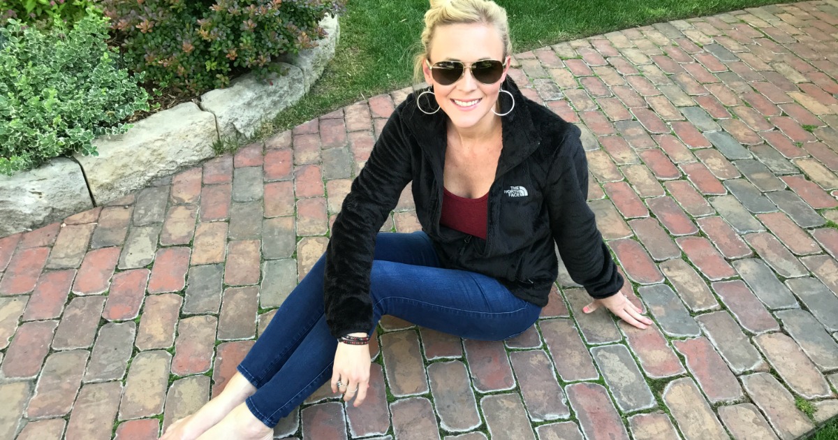 woman with sunglasses sitting on brick sidewalk