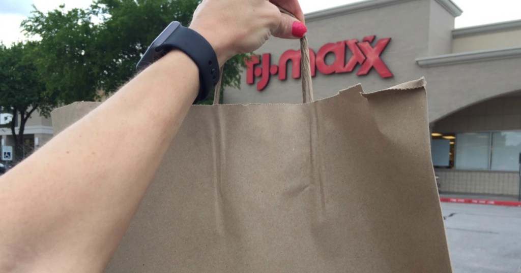 hand with brown paper shopping bag in front of T.J. Maxx store front in an outdoor shopping center