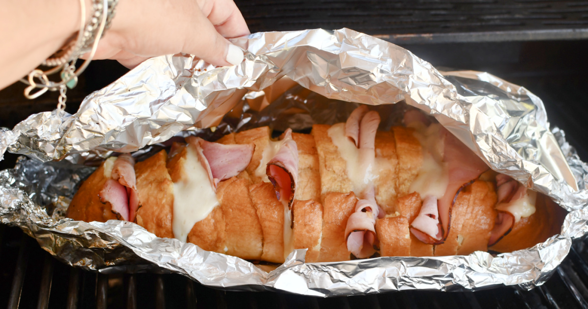 hand pulling back amazon basics aluminum foil covering ham and cheese sandwiches