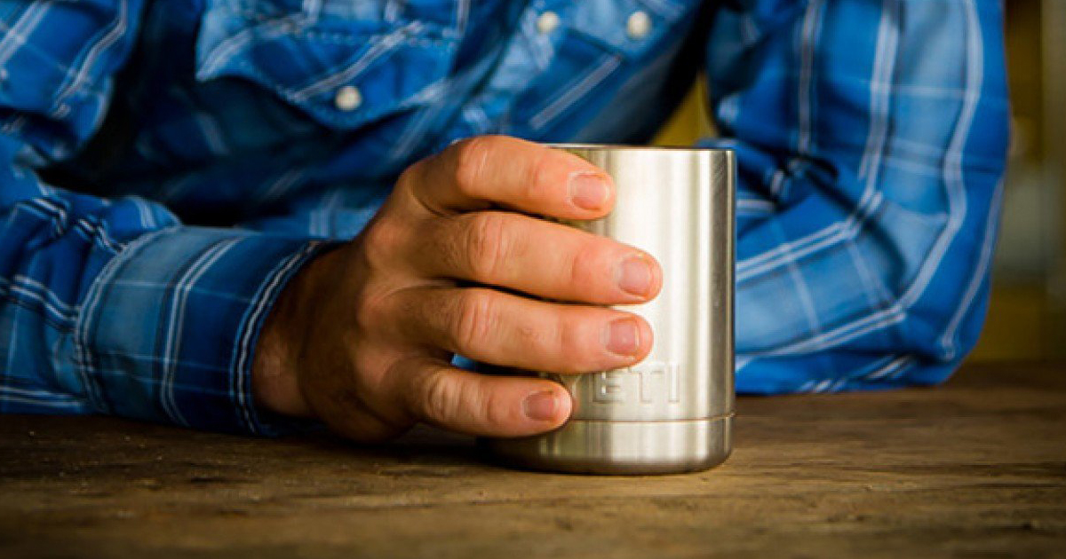 Man holding a stainless steel cup while wearing a blue rain jacket