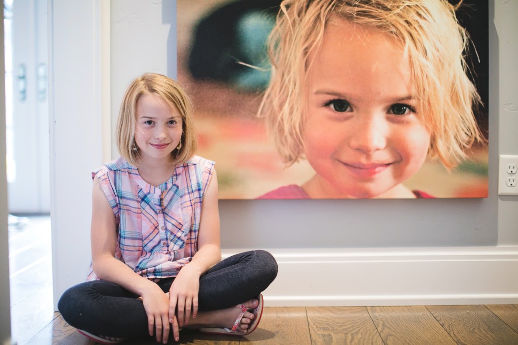 little girl sitting by canvas of herself 