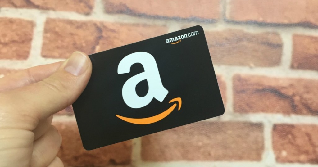Amazon gift card being held in front of a brink wall