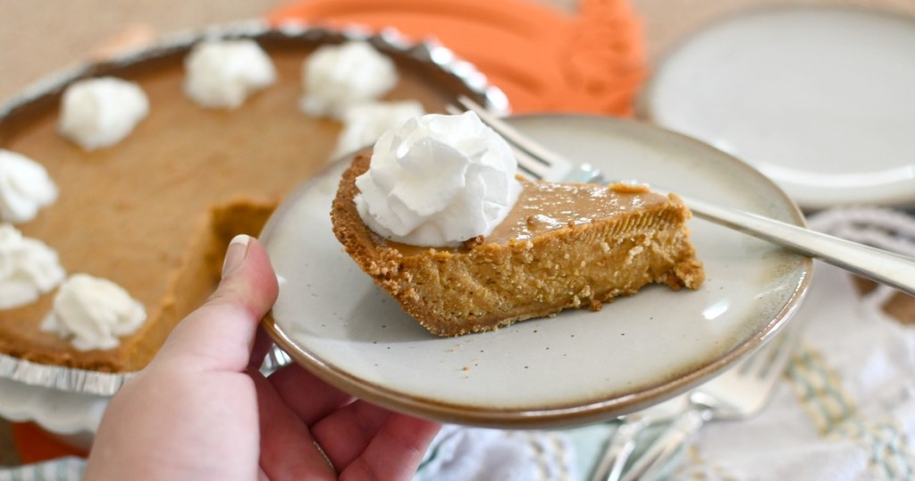 holding a plate with a slice of pumpkin pie