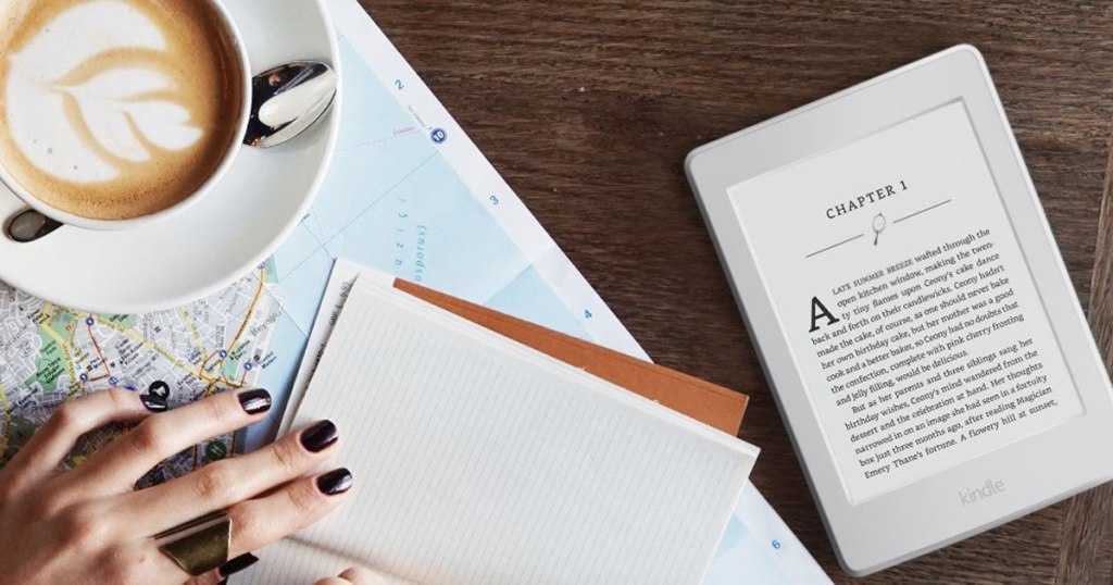 woman's hand with notebook on top of map near coffee cup and saucer and Kindle Paperwhite