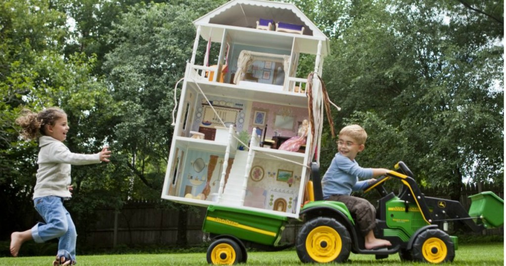boy driving a toy lawn tracker hauling a dollhouse on back