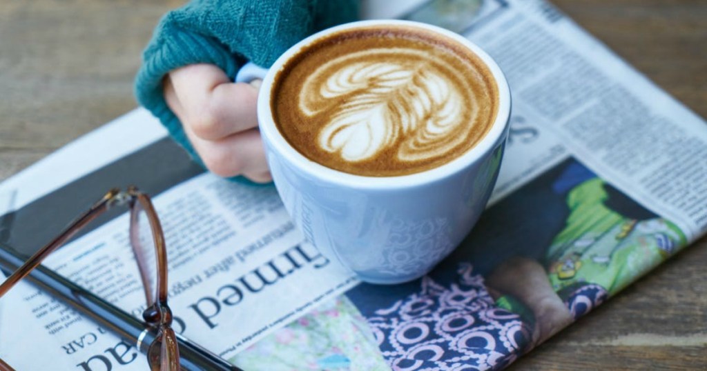 hand holding coffee on newspaper