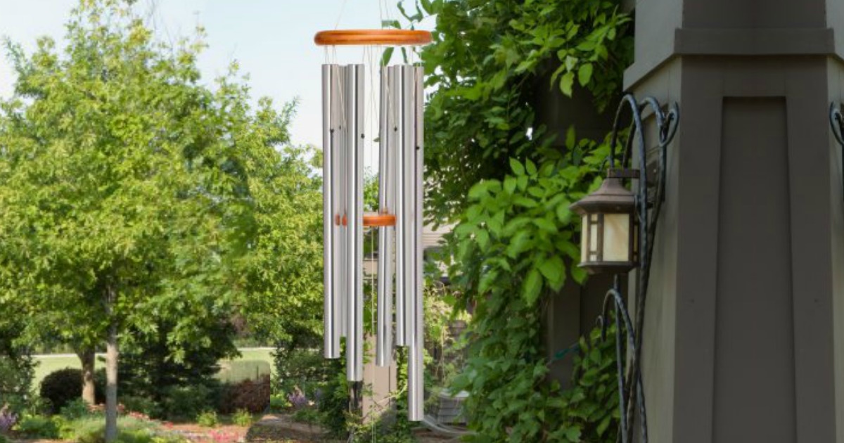 a windchime hanging outside with trees and a corner of the house in the background