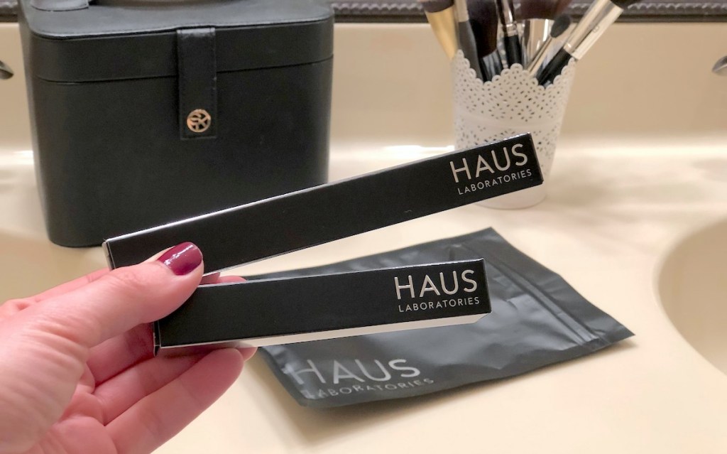 hand holding two black haus laboratories makeup products with bag and brushes in background