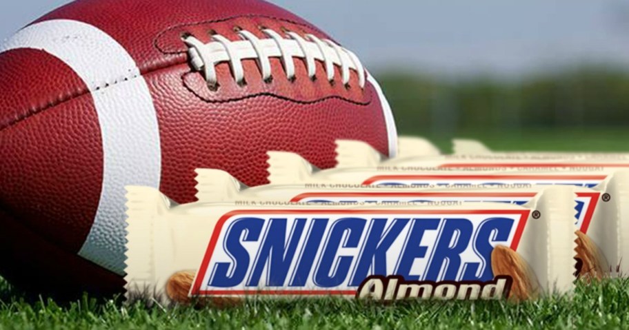 A number of Snickers bars on a field next to a football. 