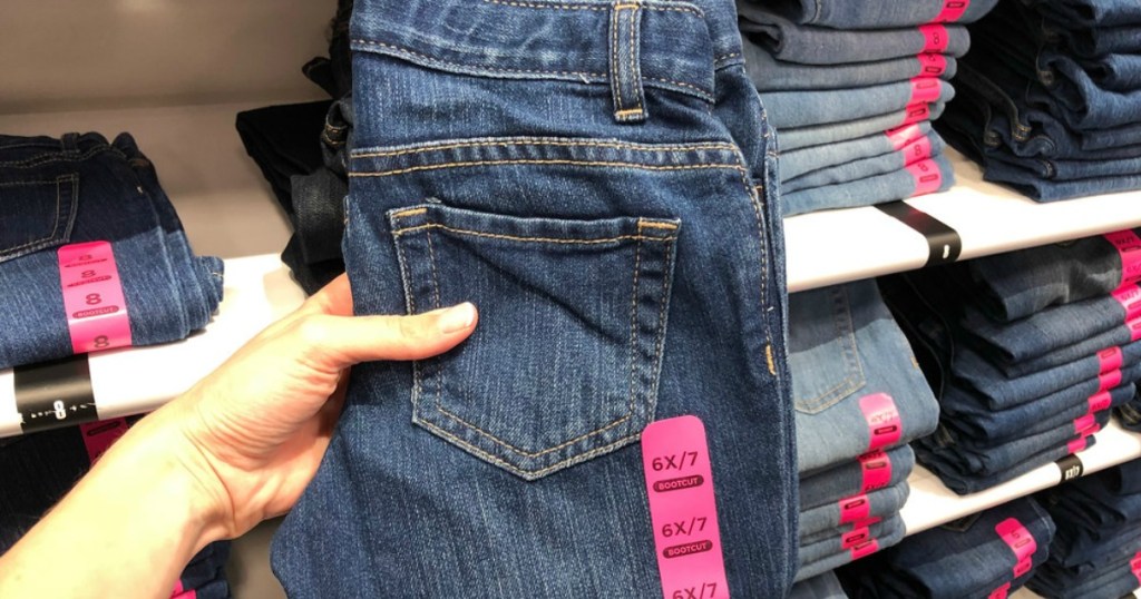 hand holding up jeans in store with jeans in background