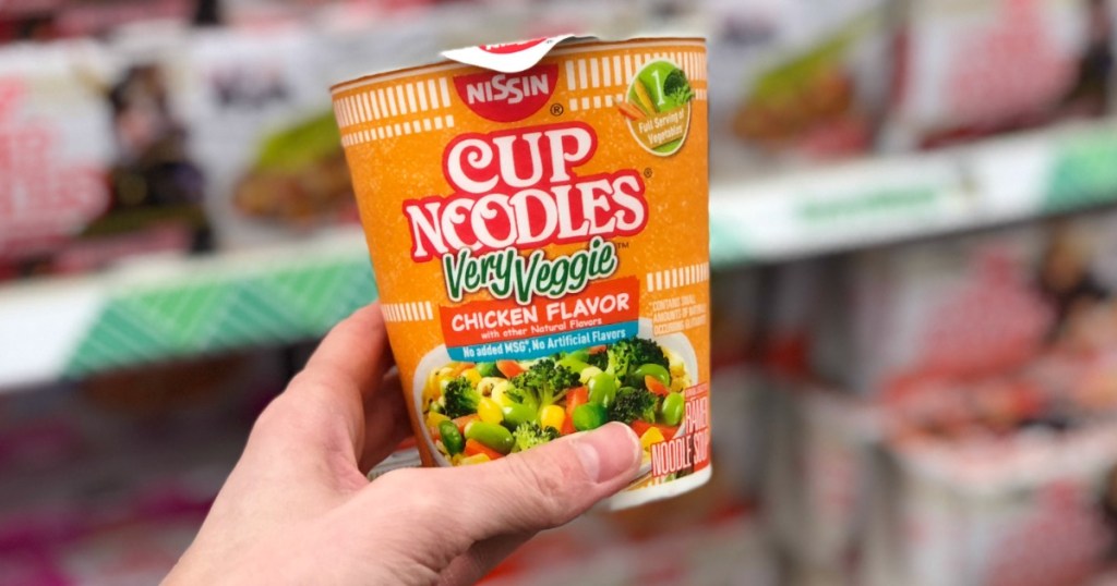 hand holding nissin cup of Noodles very veggie near in-store display