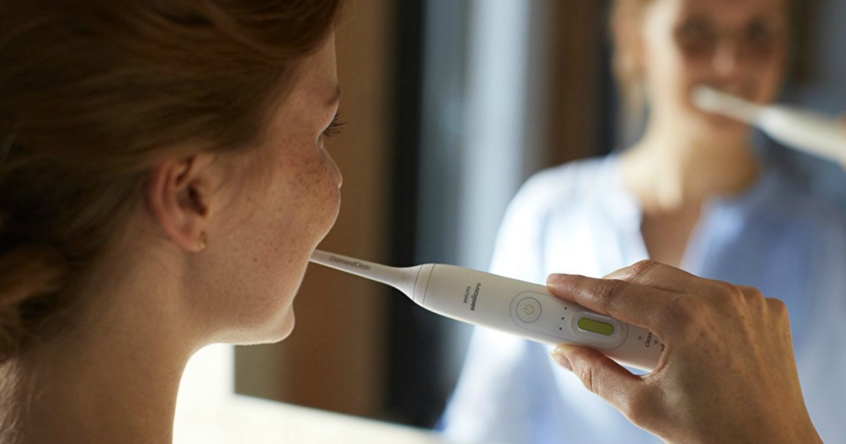 woman looking in mirror while brushing teeth with white sonicare toothbrush