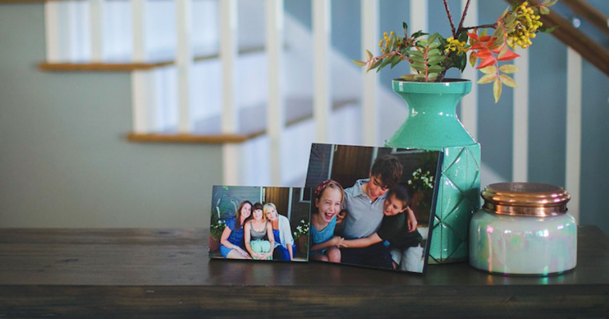 two wooden photo prints on credenza of kids laughing and women sitting together with teal vase and farmhouse stairs 