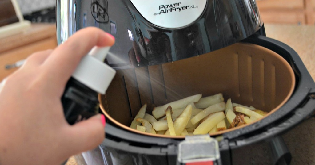 woman spraying oil into an air fryer with french fries 