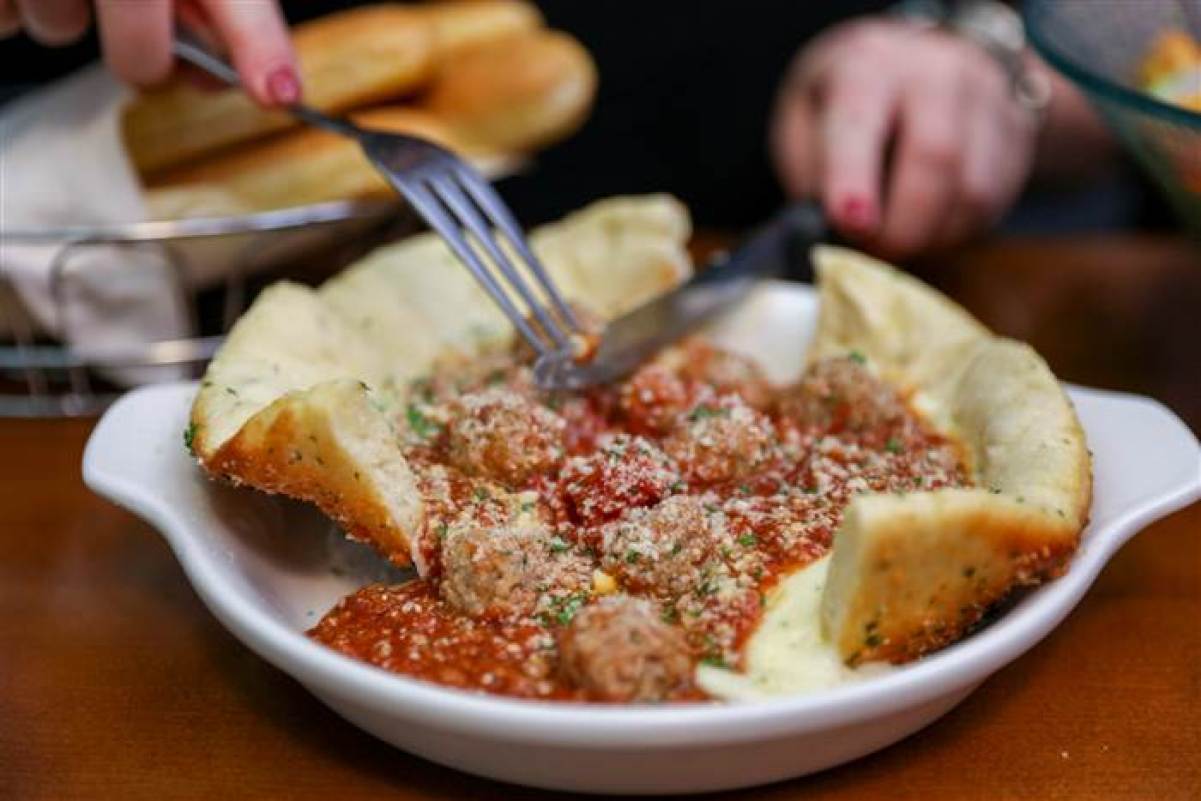 cutting an Olive Garden meatball pizza bowl with a knife and fork