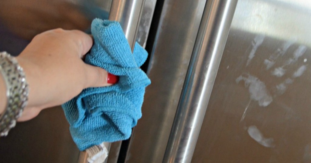 hand cleaning stainless steel fridge with blue towel 