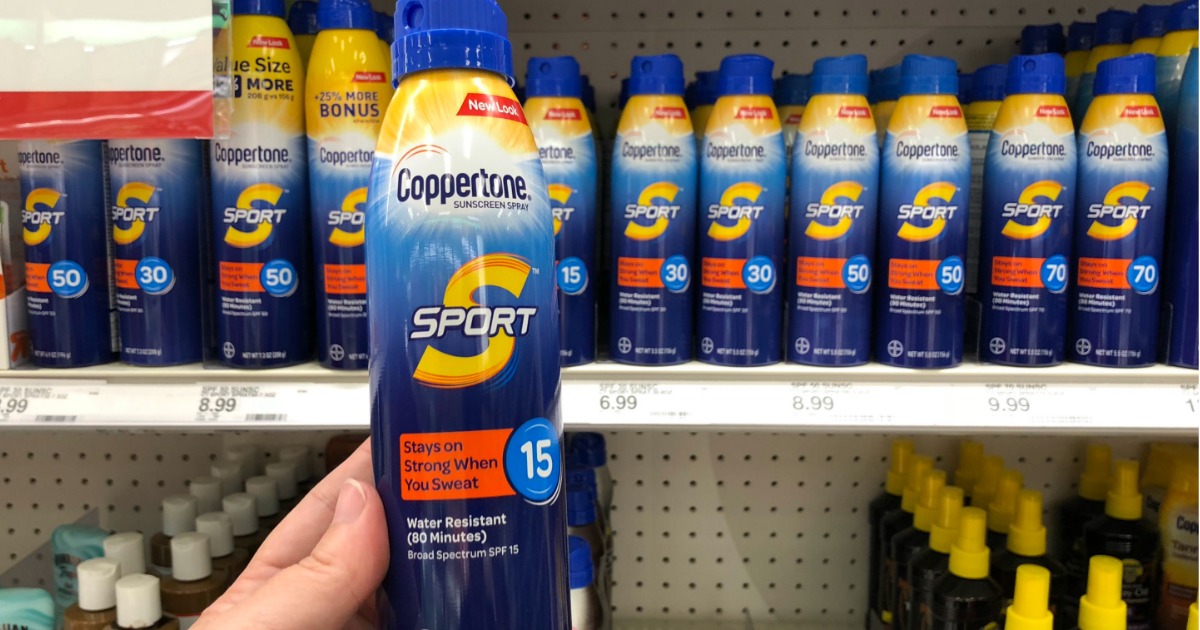 hand holding up a coppertone spray sunscreen in front of a store shelf display