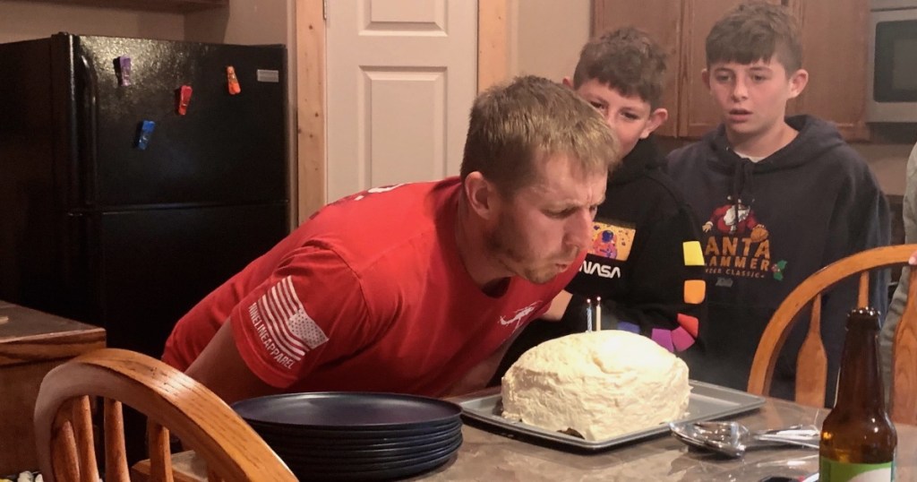 man blowing out candles on a coconut birthday cake