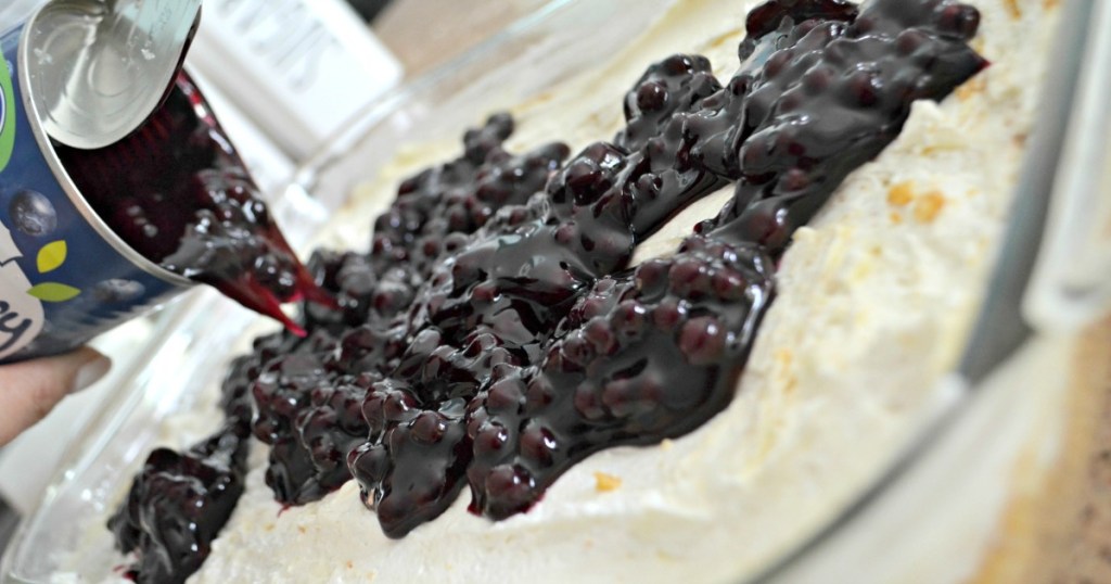 pouring blueberry pie filling over a cream cheese dessert