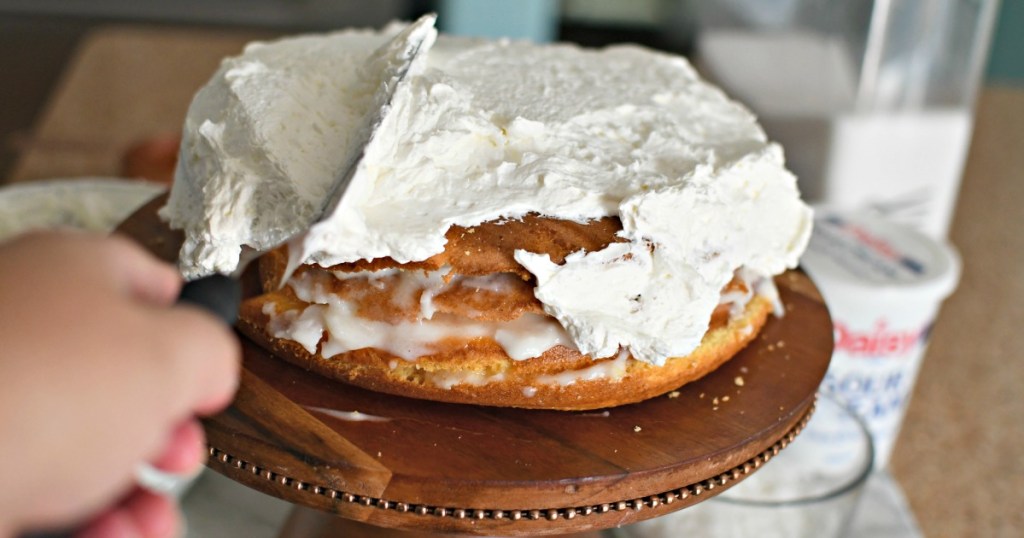 spreading whipped topping on a coconut cake