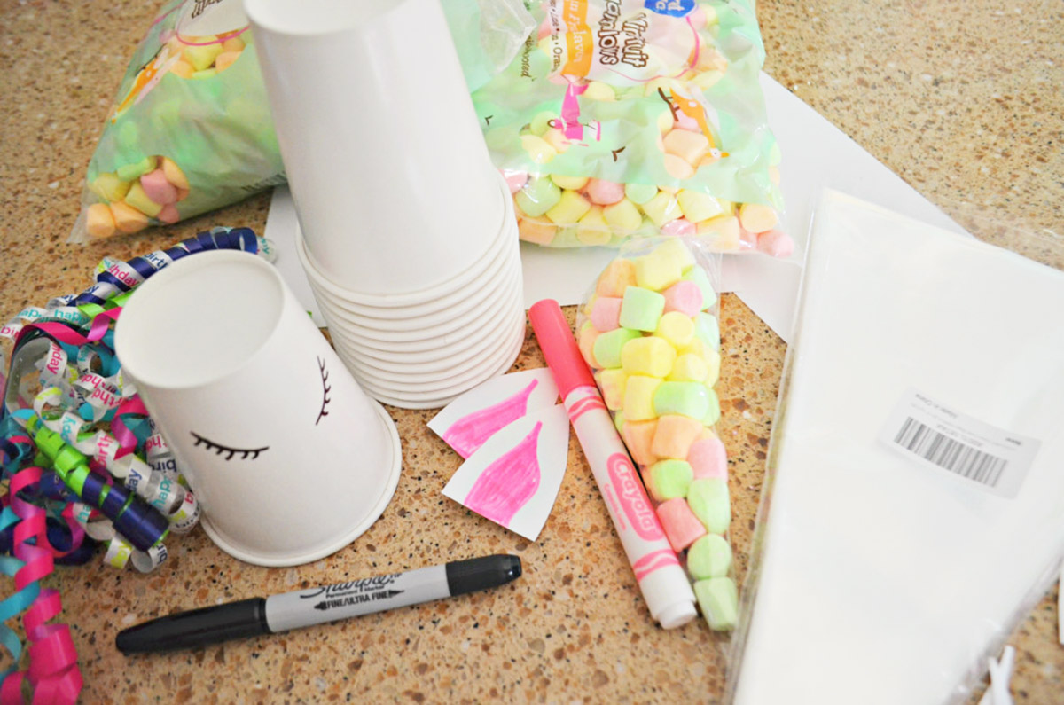 unicorn birthday party supplies with marshmallows, ribbons and cone bags on counter