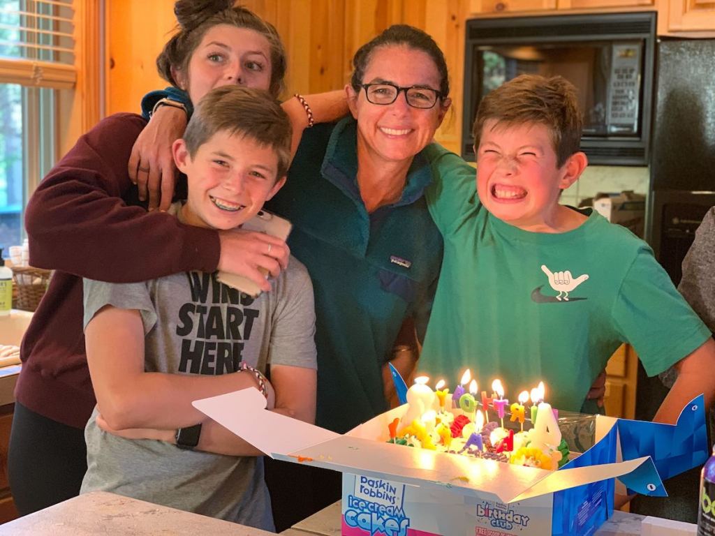 woman standing with kids in front of birthday cake with lit candles