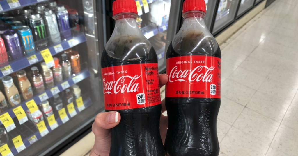 hand holding 2 bottles of coke by store display