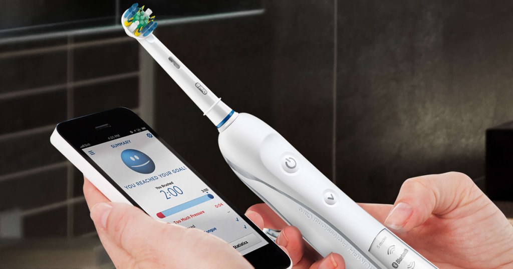 Hand holding smart phone showing an app with dental routine progress while other hand holds electric toothbrush