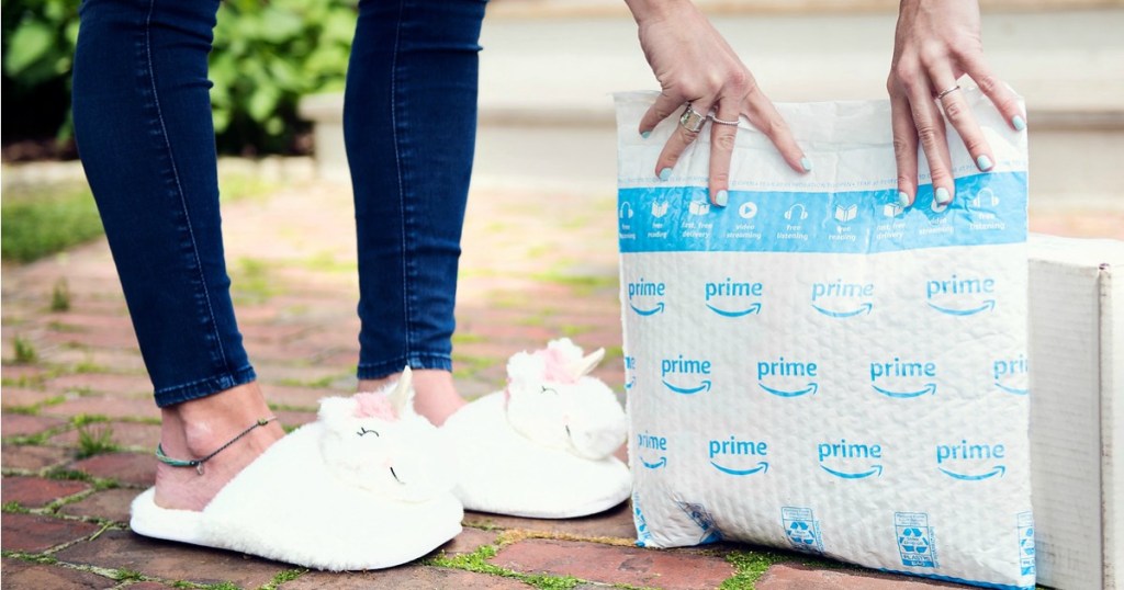 Woman wearing unicorn slippers while holding up an Amazon Prime package