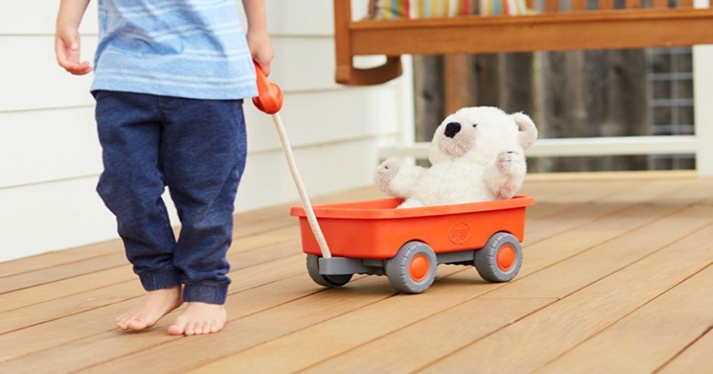little boy pulling orange wagon holding white teddy bear