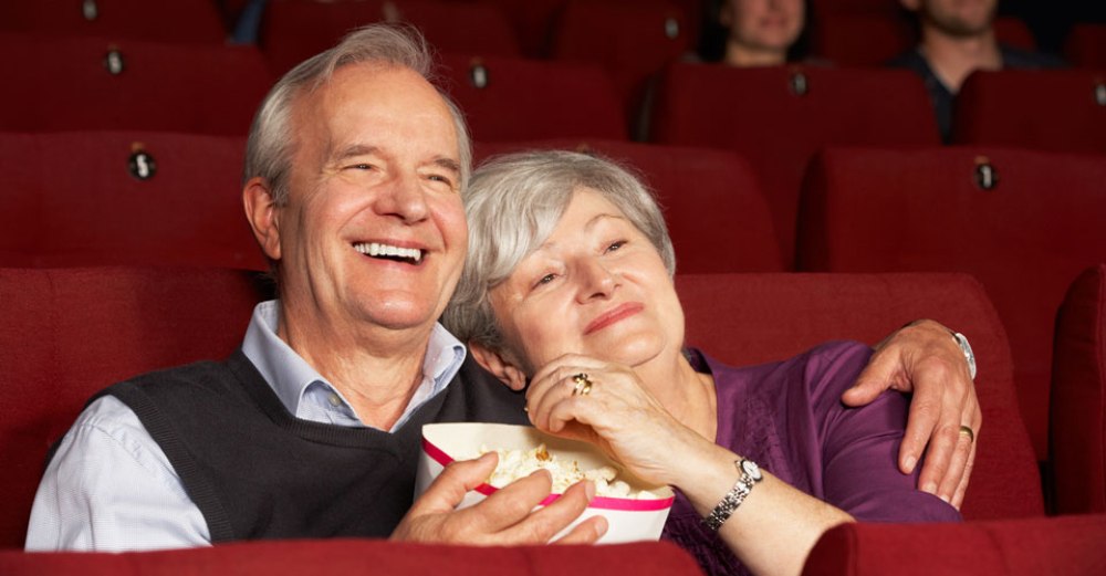 man and woman eating popcorn in a movie theater while snuggling