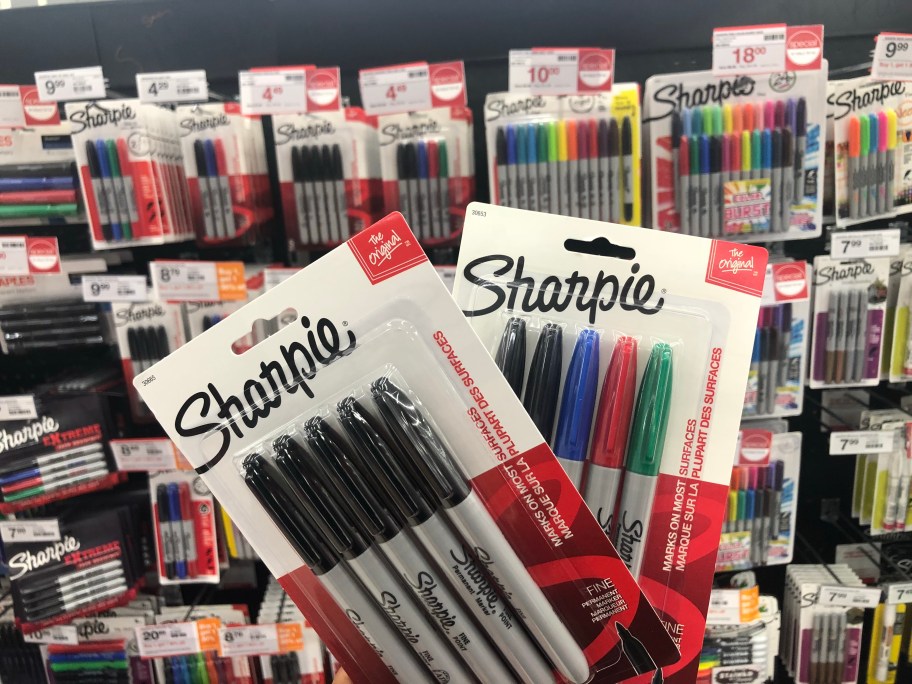 hand holding packs of Sharpie markers, more on a store display wall behind them