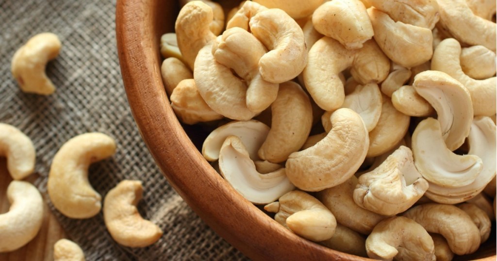 bowl full of cashews with more cashews scattered on the table next to it