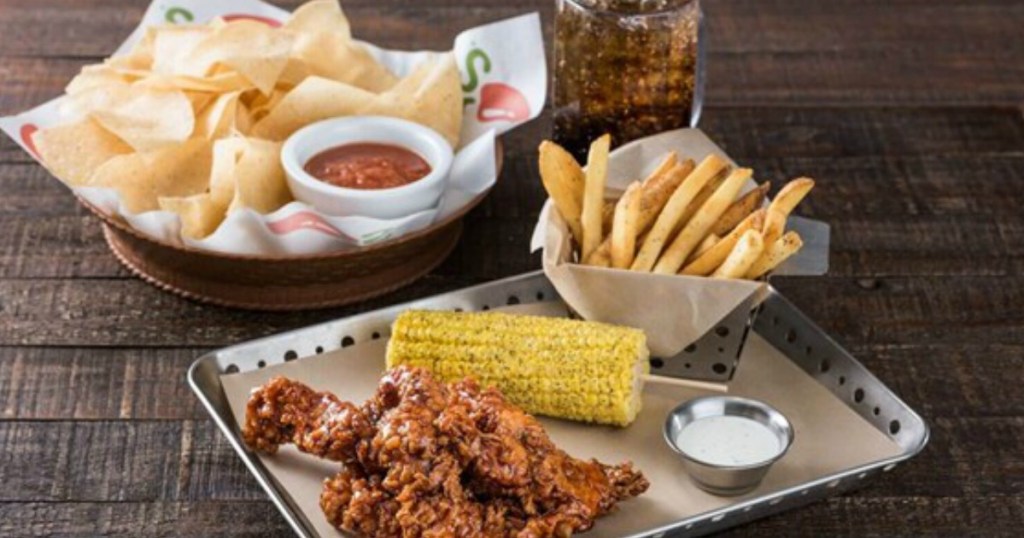 chicken crispers, corn on the cob, and fries on a tray next to chips and salsa