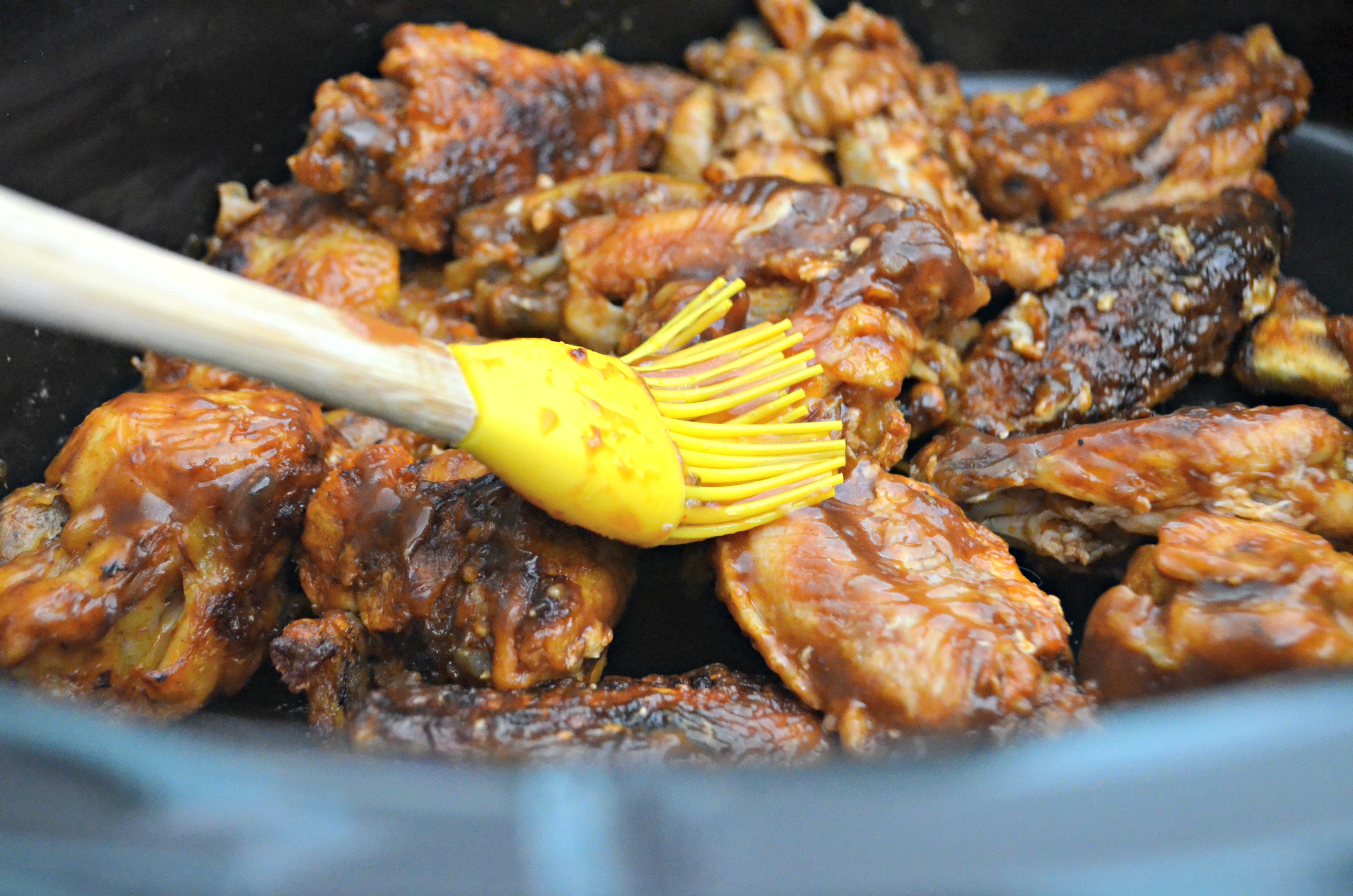 brushing on bbq sauce on chicken wings in crock-pot
