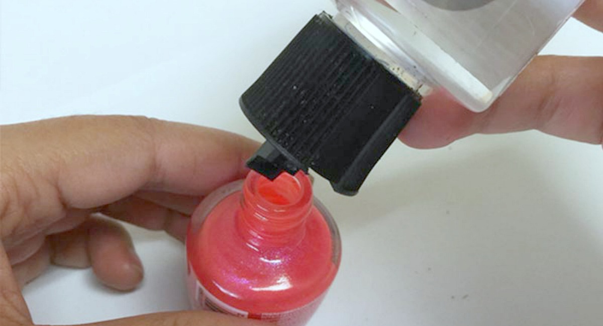 hand holding pink nail polish squirting solution into bottle