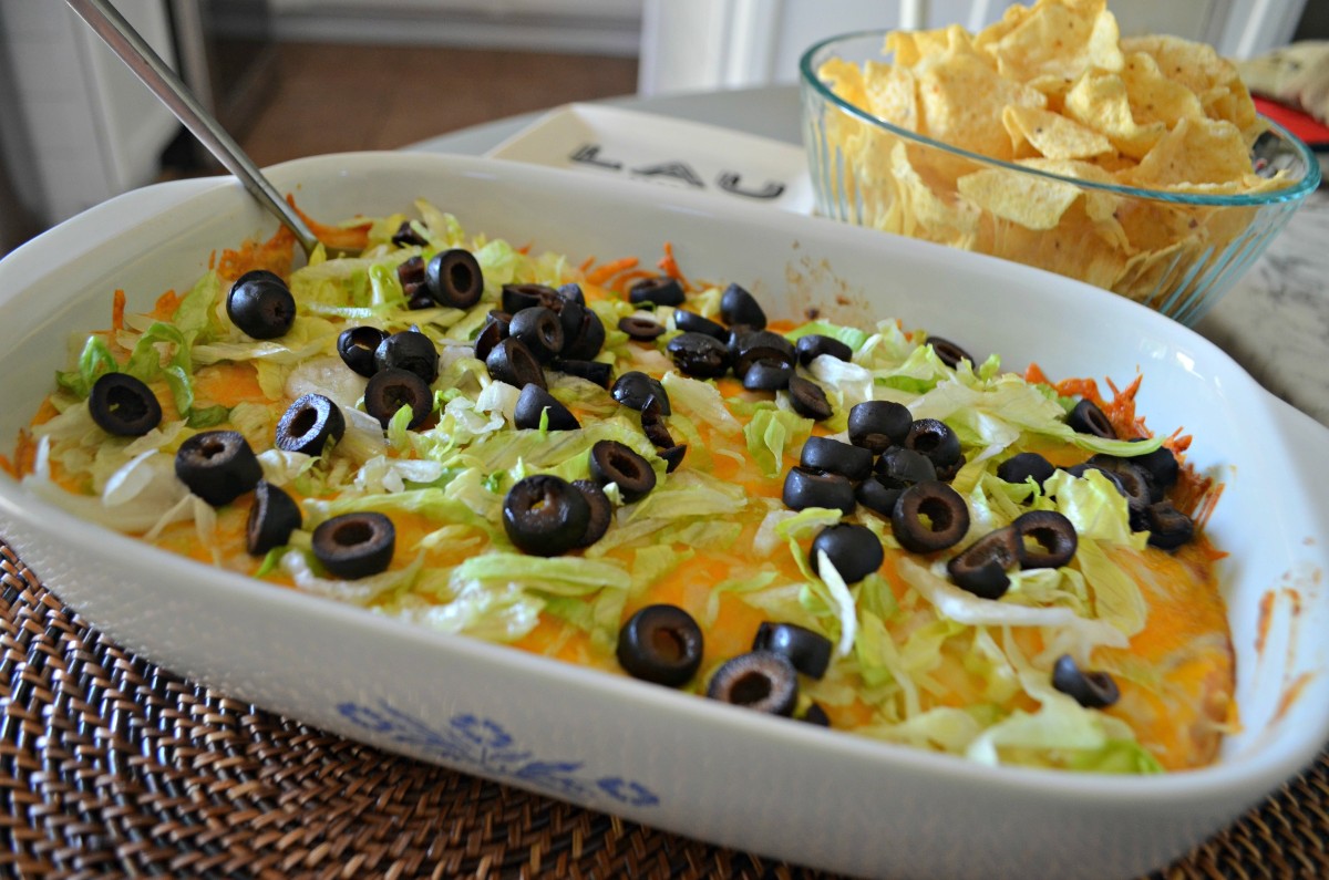 baked taco dip topped with lettuce and olives - gameday food