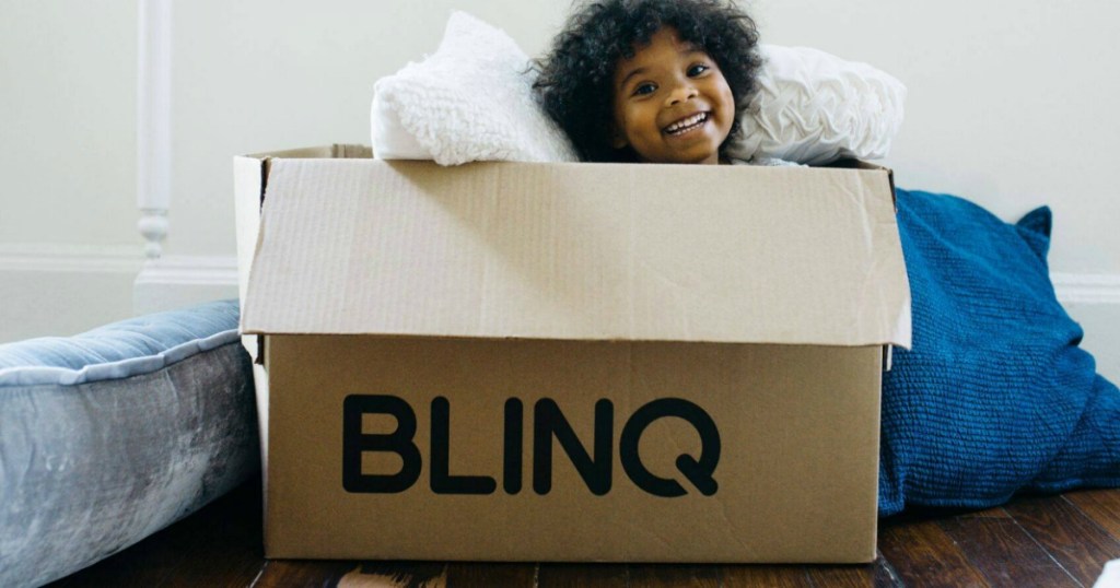 child sitting inside large BLINQ shipping box with bedding items